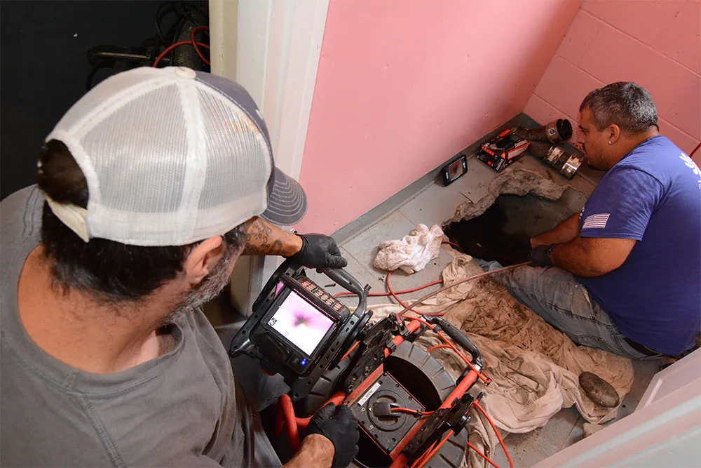 A camera technician in a workshop examining and repairing a camera lens amidst various tools and equipment.